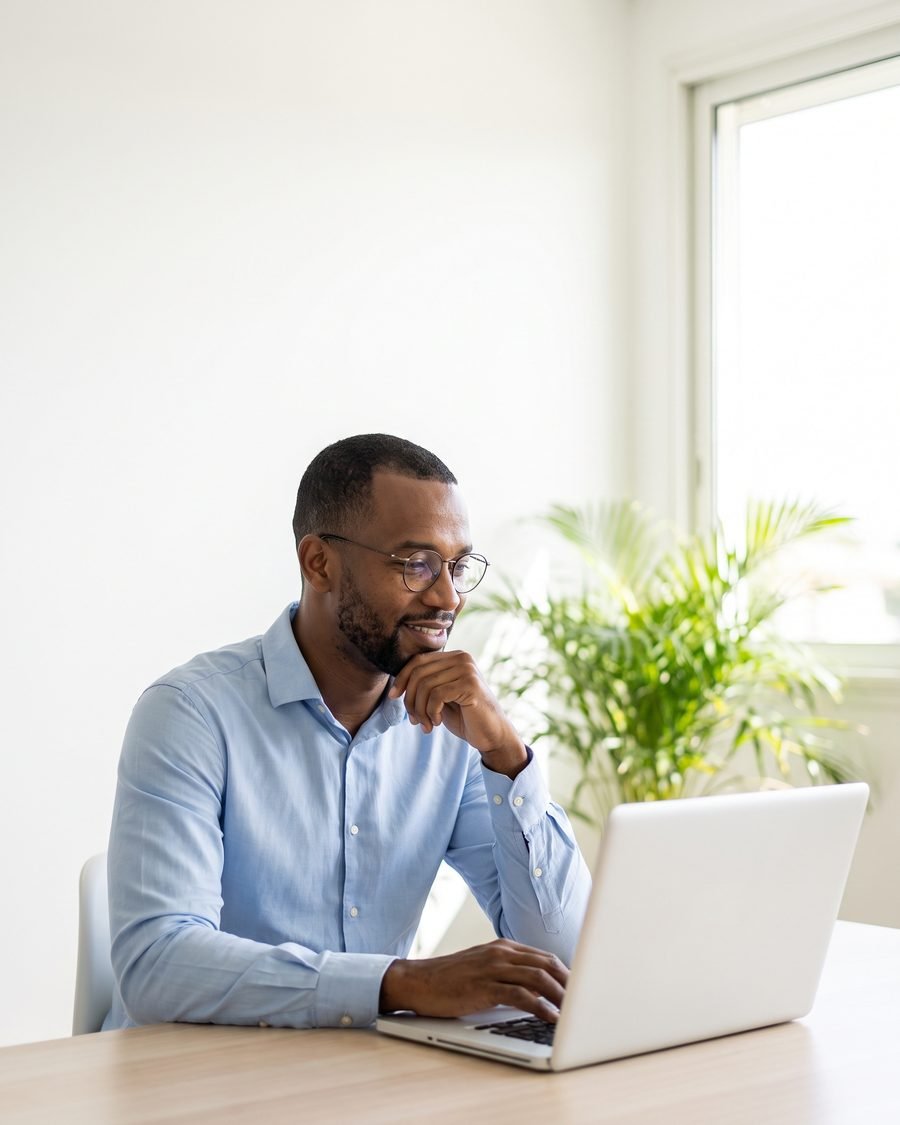 Un professionnel guadeloupéen sourit devant son ordinateur portable, dans un bureau lumineux